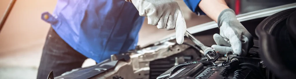 Monteur die een moersleutel gebruikt tijdens het uitvoeren van motordiagnose en reparatie onder de motorkap van een auto.